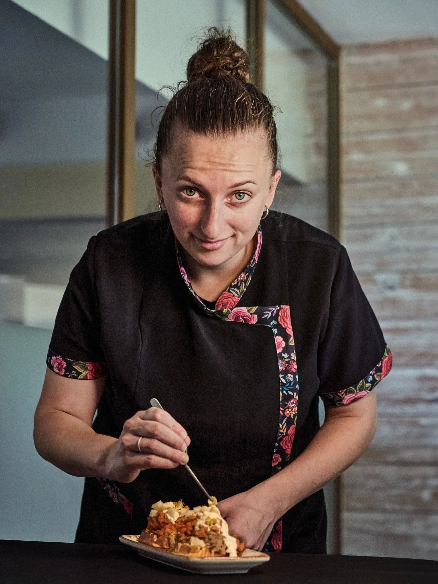 Cristina, la cocinera de Soie, emplata con pinzas y sonríe a cámara con chaquetilla negra de flores