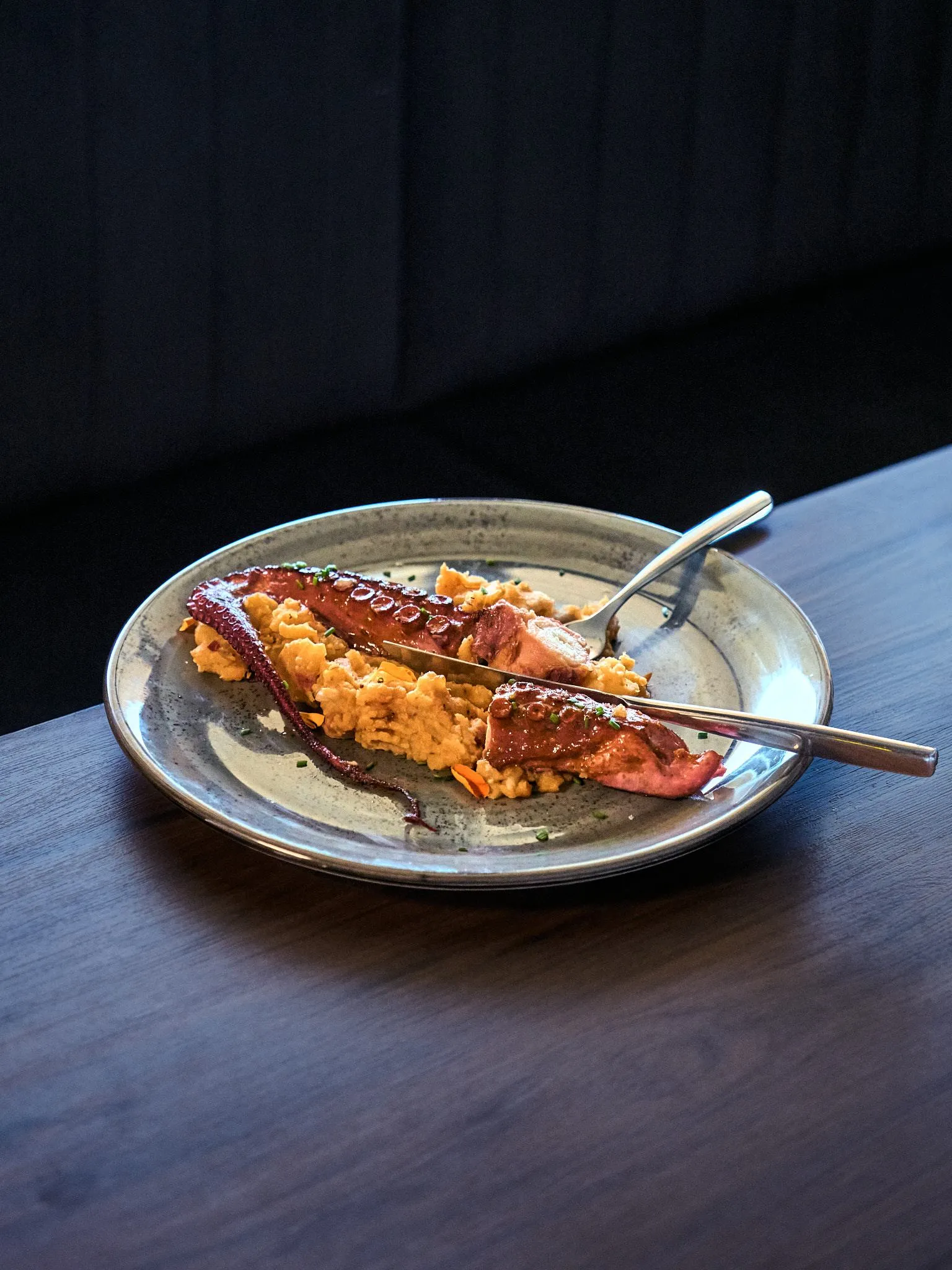 Plato de cerámica con pulpo a la brasa sobre un cremoso, con tenedor y cuchara