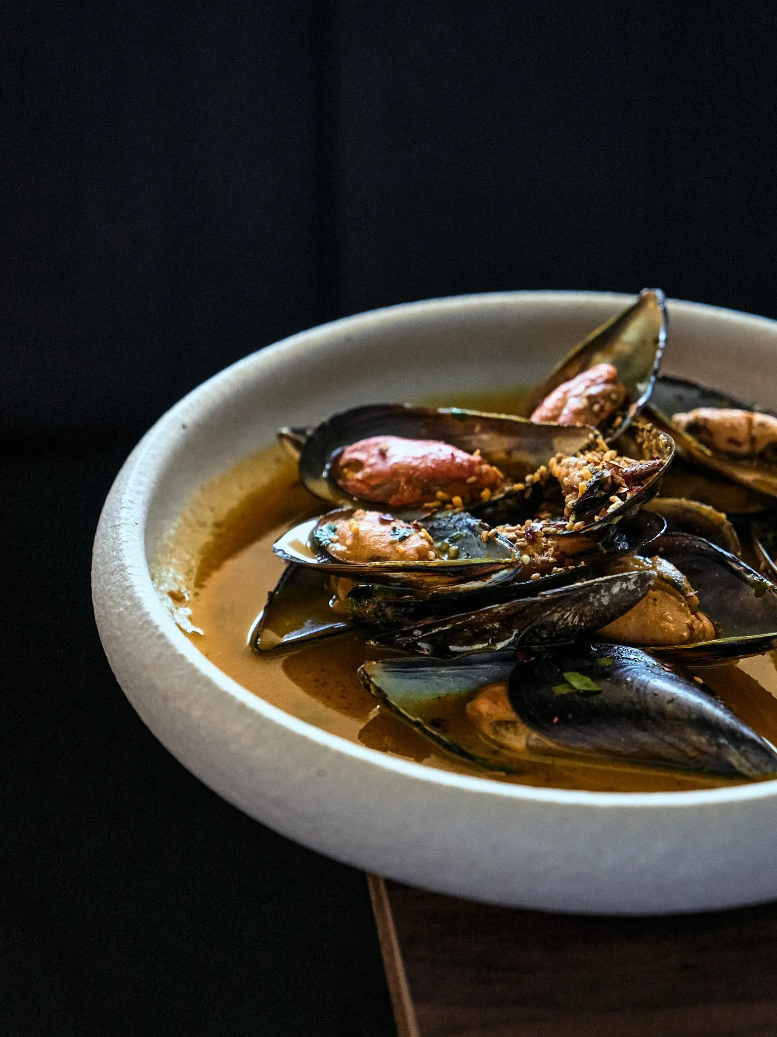 Cuenco blanco con mejillones en salsa sobre una mesa de madera oscura